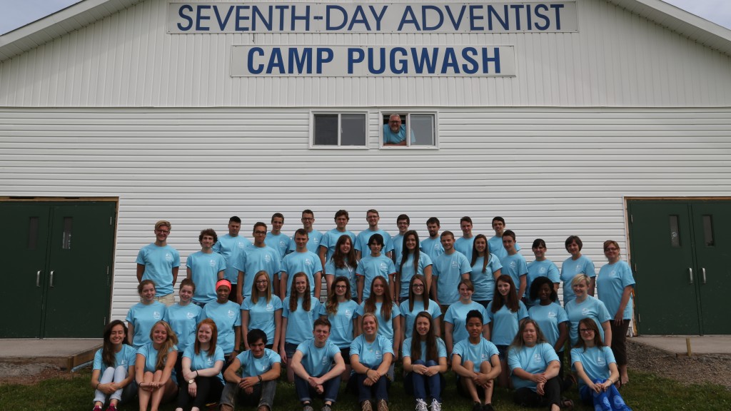Group photo of the 2015 camp staff in front of the auditorium with Pastor Paul sticking his head out of the window above the group.